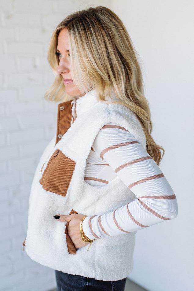 Woman wearing a white fleece vest with brown accents against a plain background