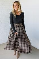 Woman wearing a black top and plaid skirt against a white brick wall.