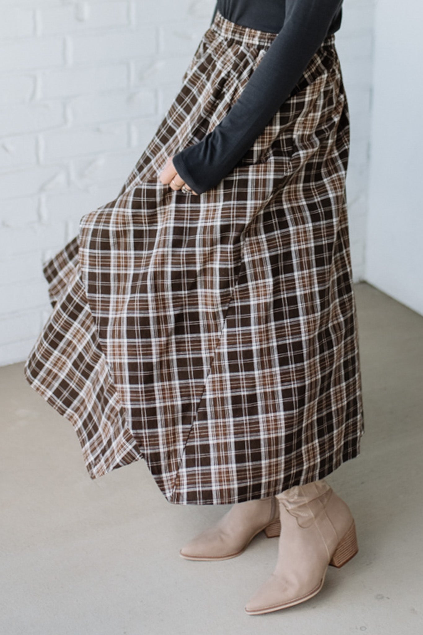Person wearing a plaid skirt and beige boots against a white brick wall.