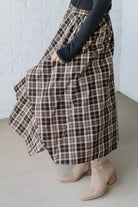 Person wearing a plaid skirt and beige boots against a white brick wall.