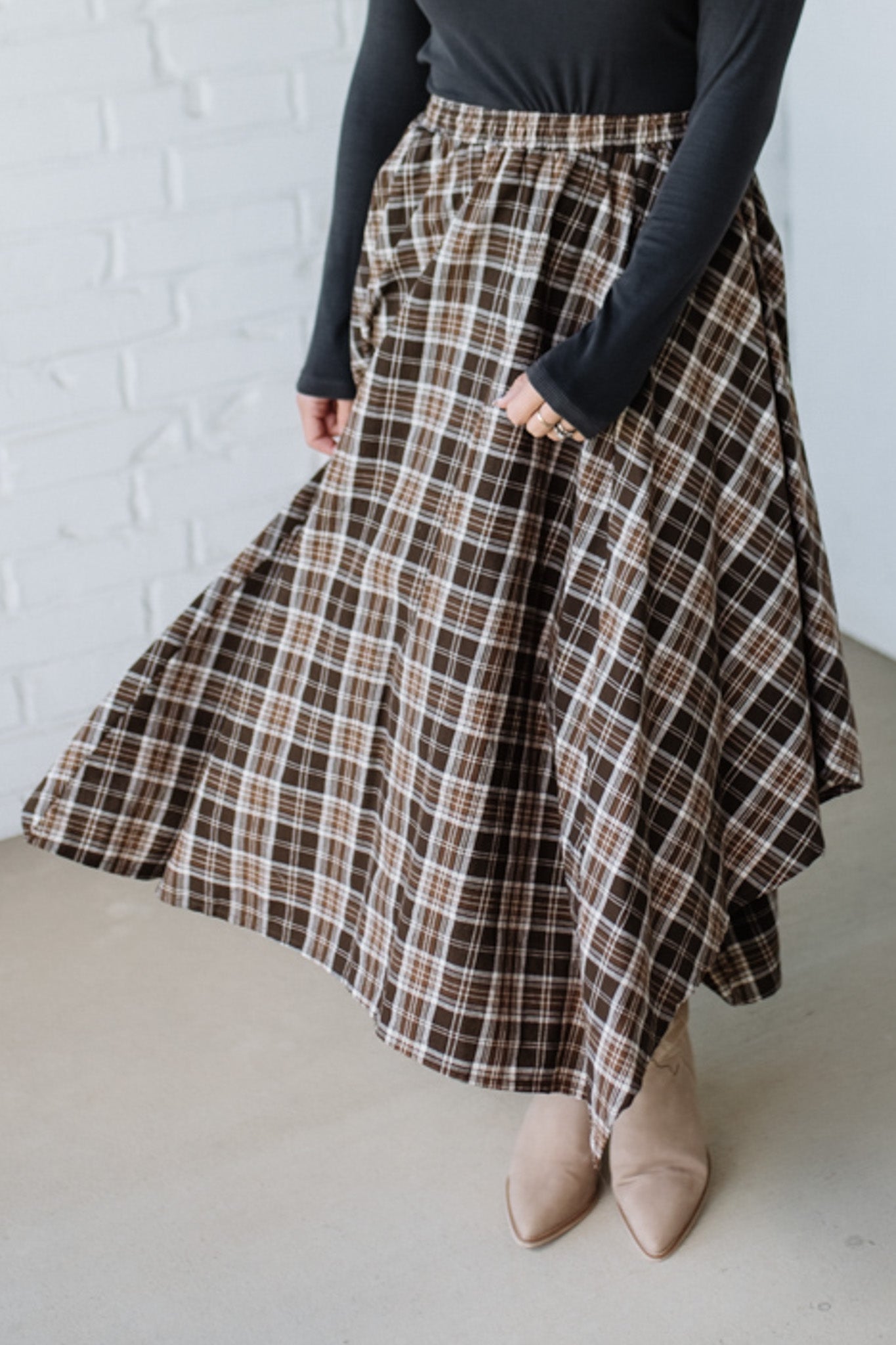 Person wearing a plaid skirt with a white brick wall background