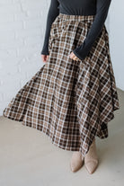 Person wearing a plaid skirt with a white brick wall background