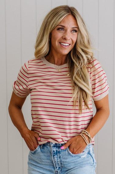 Woman wearing a red and white striped shirt with blue jeans against a light wooden panel background