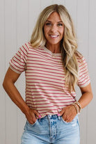 Woman wearing a red and white striped shirt and blue jeans against a light wooden panel background