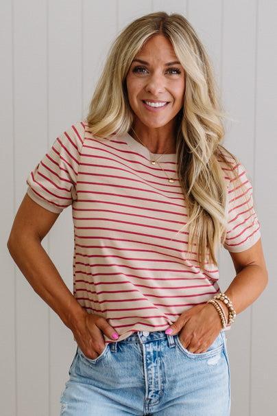 Woman wearing a red and white striped shirt and blue jeans against a light wooden panel background