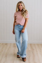 Woman wearing a striped shirt and jeans standing against a white paneled wall.