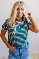 Woman wearing a striped shirt and jeans, smiling and posing with one hand on her hair.