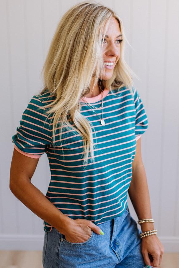 Woman wearing a green and white striped shirt with denim shorts, standing against a plain background.