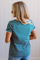 Person wearing a blue and green striped shirt with pink trim against a white paneled wall.