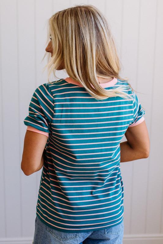 Person wearing a blue and green striped shirt with pink trim against a white paneled wall.