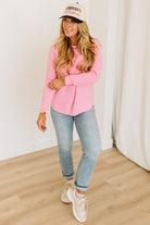 Blonde woman wearing jeans and a pink sweater with a black and white hat and sneakers.