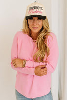 Blonde woman wearing jeans and a pink sweater with a black and white hat and sneakers.