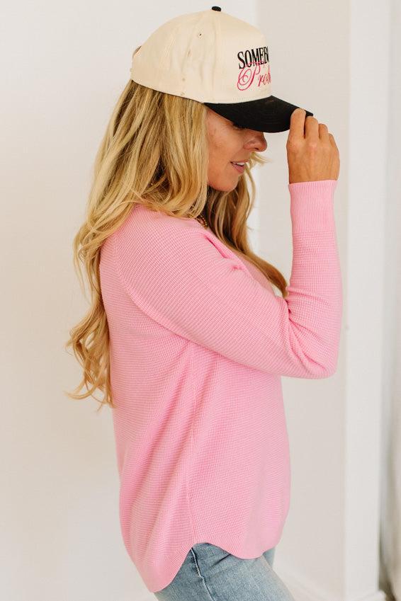 Blonde woman wearing jeans and a pink sweater with a black and white hat and sneakers.