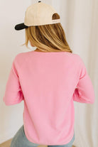 Blonde woman wearing jeans and a pink sweater with a black and white hat and sneakers.