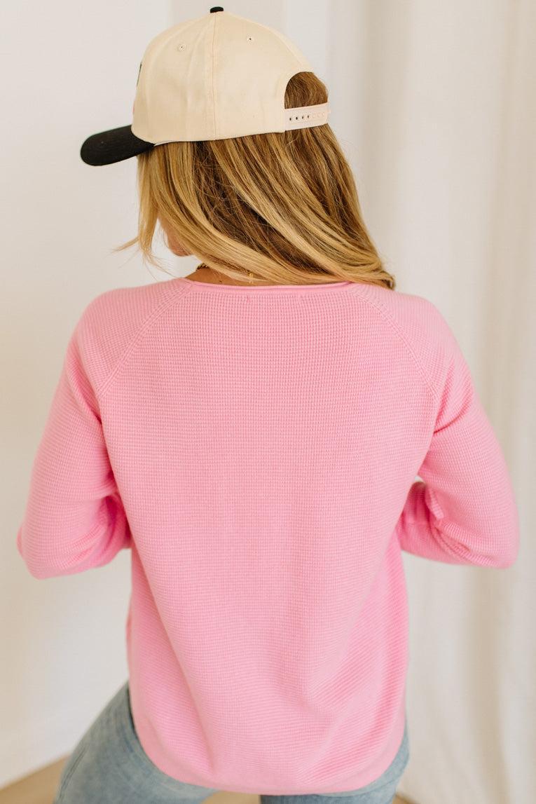 Blonde woman wearing jeans and a pink sweater with a black and white hat and sneakers.