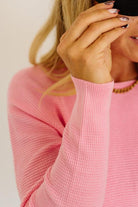 Blonde woman wearing jeans and a pink sweater with a black and white hat and sneakers.