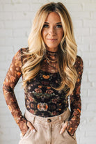 Woman wearing a floral long-sleeve top against a white brick wall