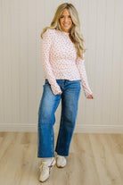 Woman wearing a polka dot blouse and blue jeans standing against a light wooden paneled wall.