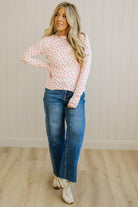 Woman wearing a polka dot blouse and jeans standing against a white paneled wall.
