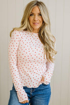 Woman wearing a white long-sleeve top with red patterns and blue jeans against a neutral background