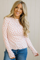 Woman wearing a white long-sleeve top with red patterns and blue jeans against a light background