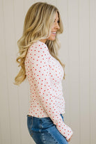 Woman wearing a white blouse with red polka dots and blue jeans against a beige wall.