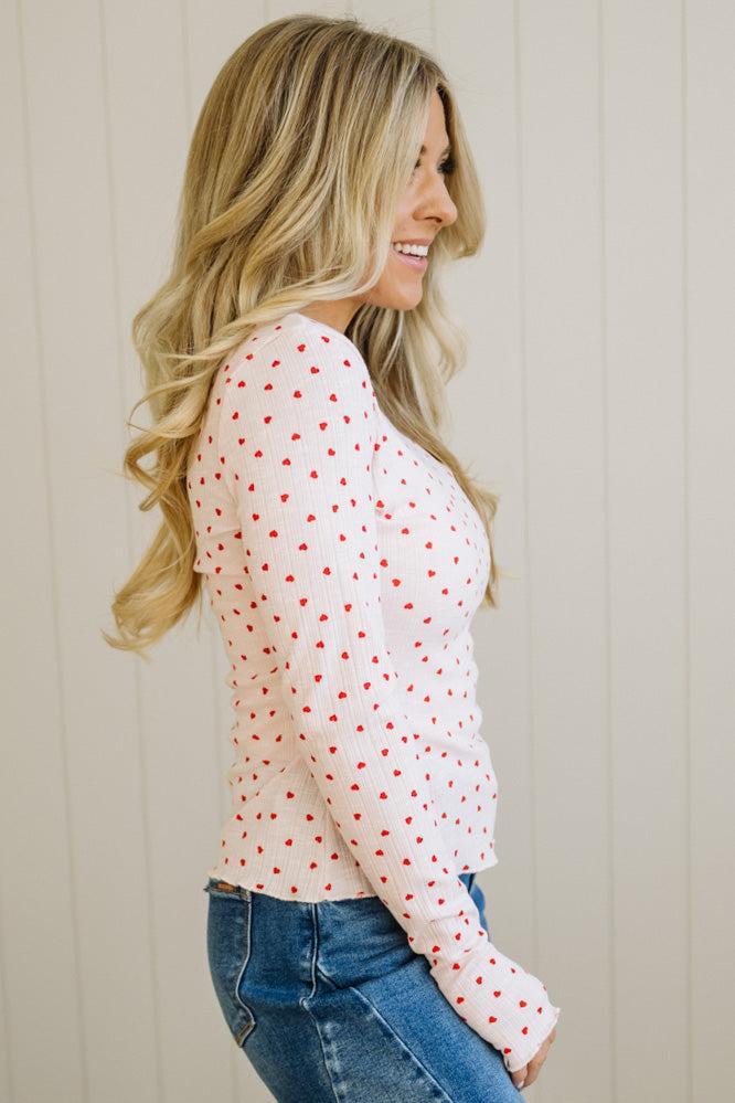 Woman wearing a white blouse with red polka dots and blue jeans against a beige wall.