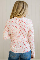 Person wearing a white blouse with red polka dots and blue jeans against a light wooden panel background