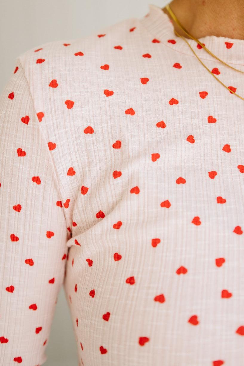 Close-up of a person wearing a white long-sleeve shirt with red heart patterns.