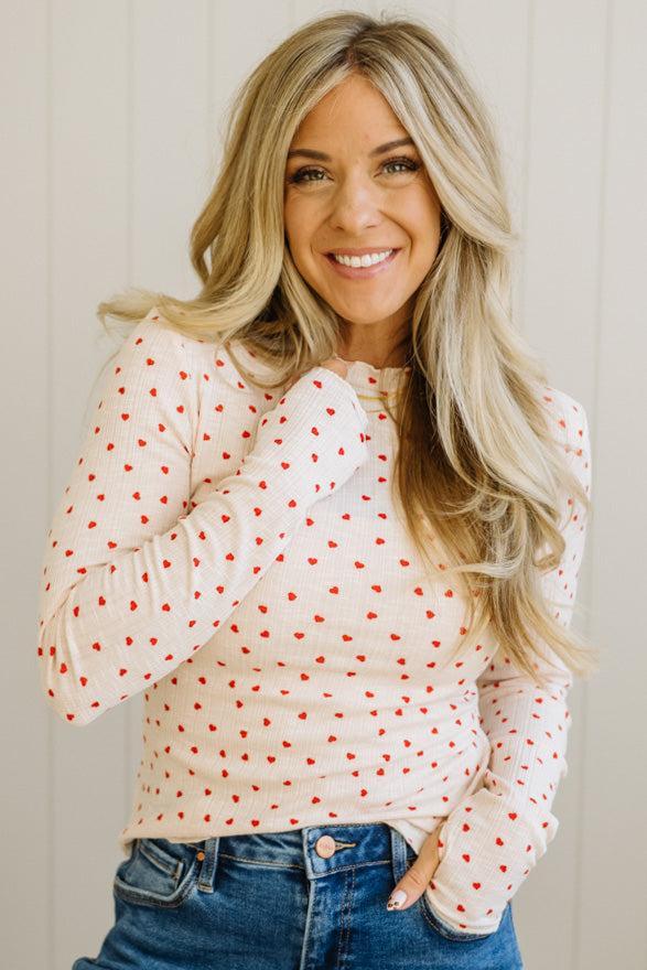 Woman wearing a white blouse with red polka dots and blue jeans against a plain background