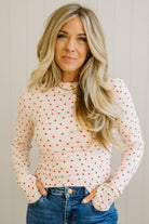 Woman wearing a white long-sleeve top with red polka dots and blue jeans against a neutral background