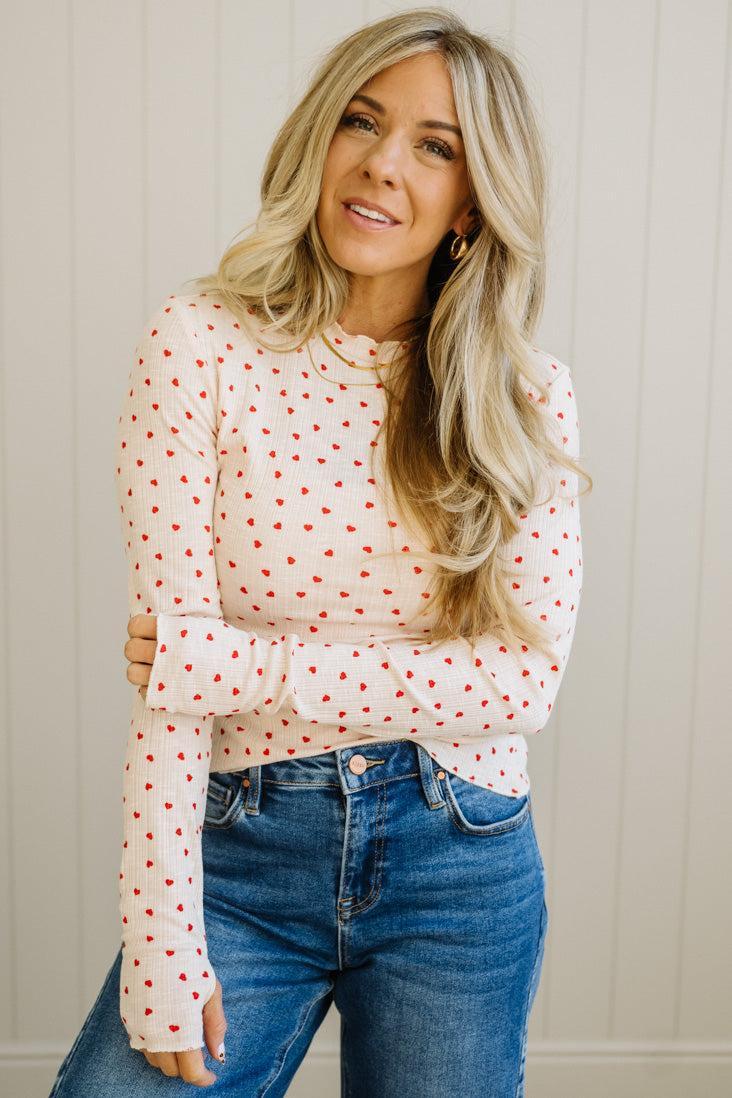 Woman wearing a white blouse with red polka dots and blue jeans against a neutral background