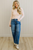 Woman wearing a polka dot blouse and blue jeans standing against a neutral wall.