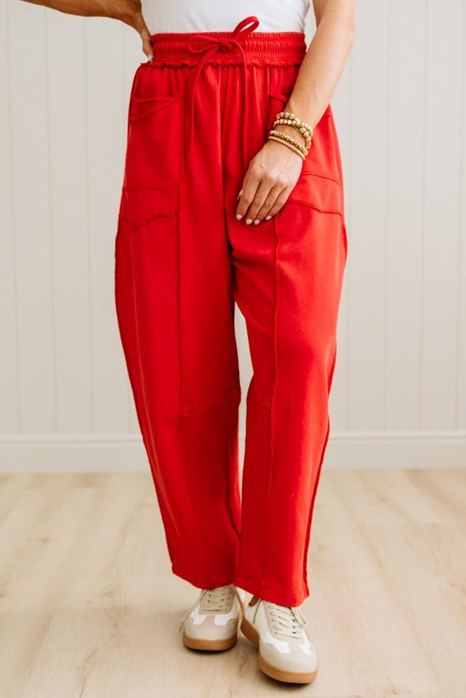 Person wearing red pants and white sneakers on a light wooden floor.