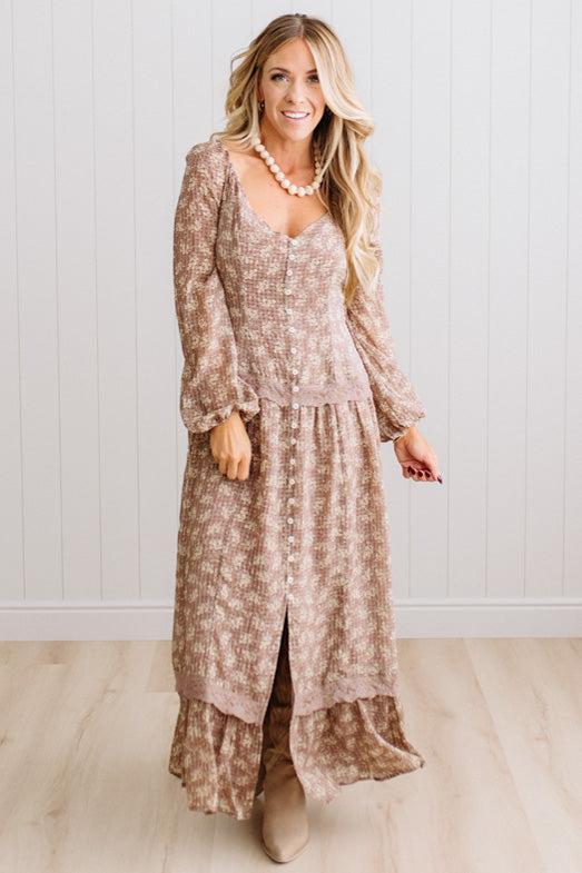 Latte brown colored Floral Drop Waist Maxi Dress on a blonde woman with a large white beaded necklace.