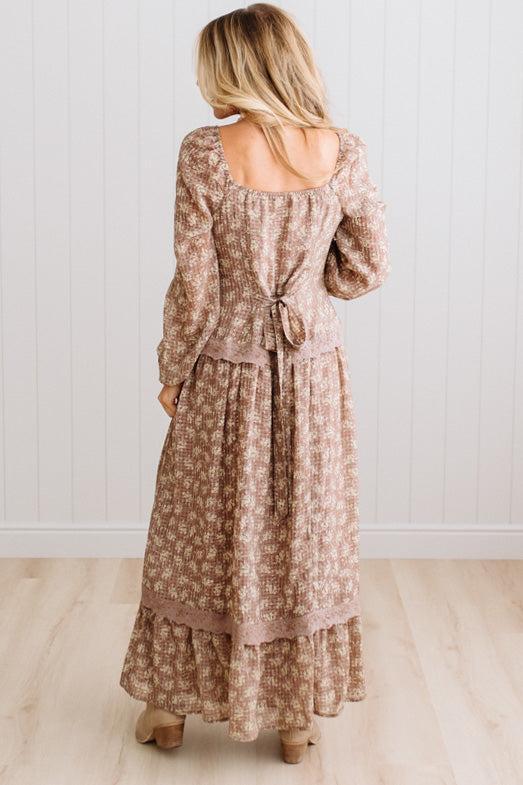 Latte brown colored Floral Drop Waist Maxi Dress on a blonde woman with a large white beaded necklace.