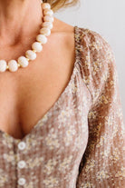 Latte brown colored Floral Drop Waist Maxi Dress on a blonde woman with a large white beaded necklace.