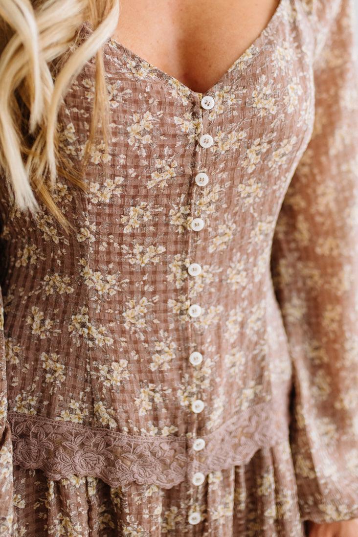 Latte brown colored Floral Drop Waist Maxi Dress on a blonde woman with a large white beaded necklace.