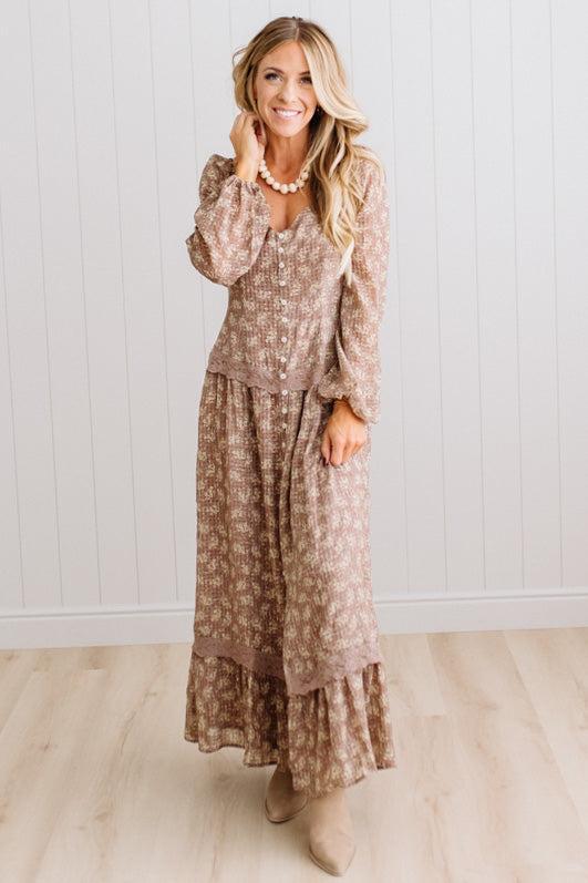 Latte brown colored Floral Drop Waist Maxi Dress on a blonde woman with a large white beaded necklace.
