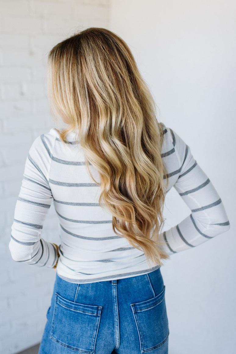 Person wearing a striped long-sleeve top and blue jeans with a plain background