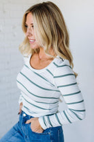 Woman wearing a striped long-sleeve top and blue jeans against a light background