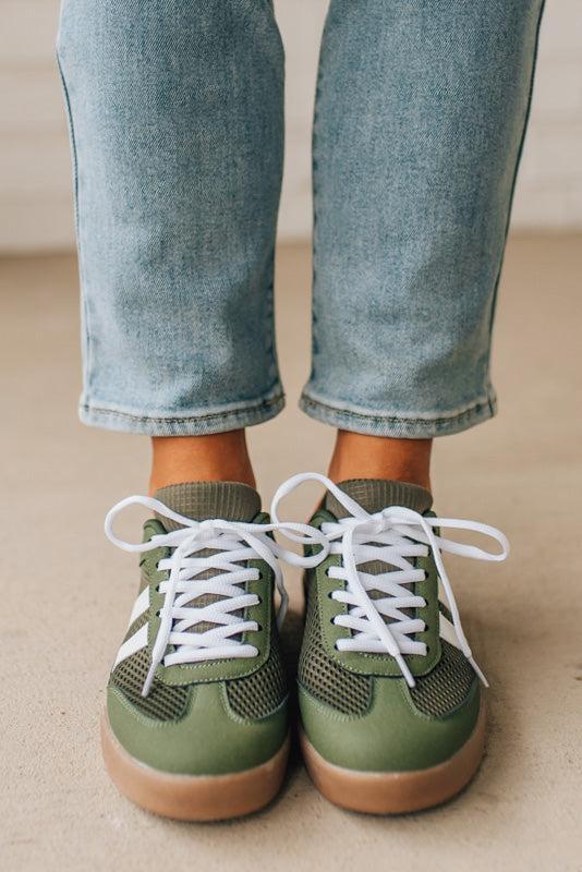 Green sneakers with white laces worn with light blue jeans on a neutral background