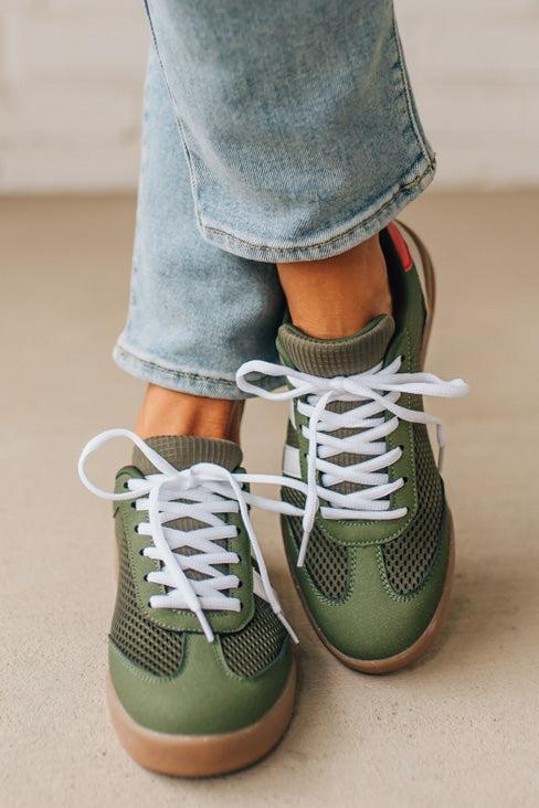 Green sneakers with white laces worn with light blue jeans on a neutral background