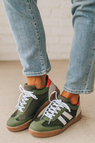 Green sneakers with white laces worn with light blue jeans on a neutral background