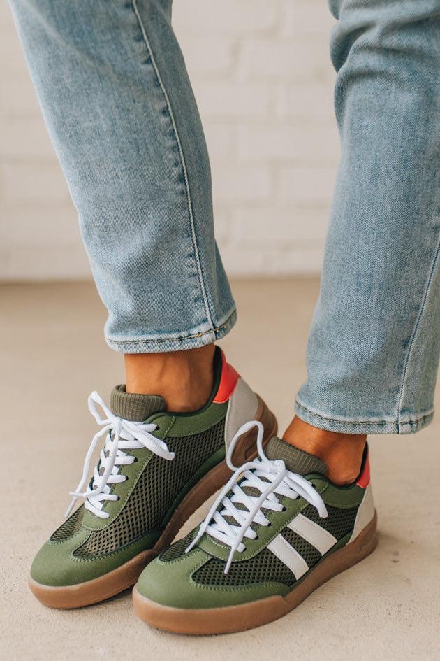 Green sneakers with white laces worn with light blue jeans on a neutral background