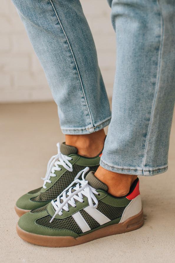 Green sneakers with white laces worn with light blue jeans on a neutral background
