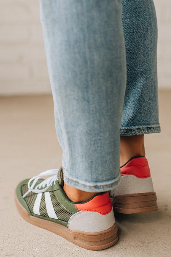 Close-up of a person wearing colorful sneakers with jeans on a neutral background