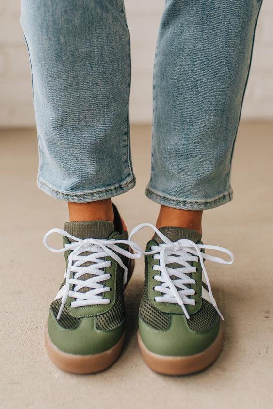 Green sneakers with white laces worn with light blue jeans on a neutral background