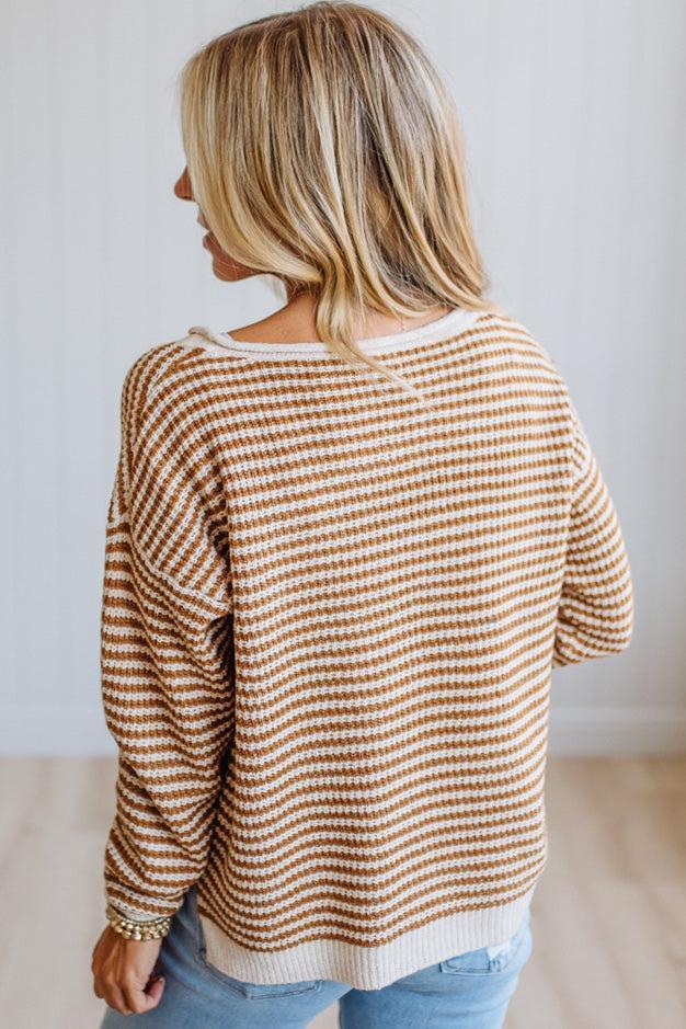 A woman shown from the back wearing a waffle-knit long-sleeve sweater with horizontal brown and cream stripes, paired with light blue jeans.