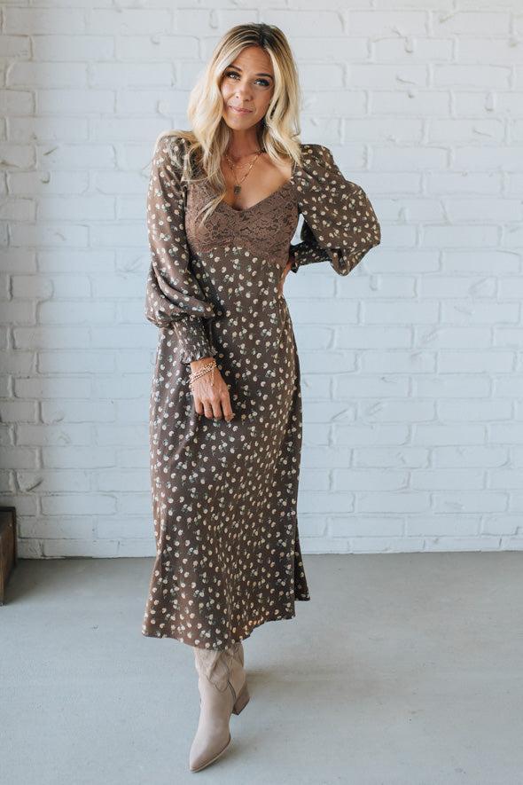Woman wearing a patterned dress with puff sleeves against a white brick wall.